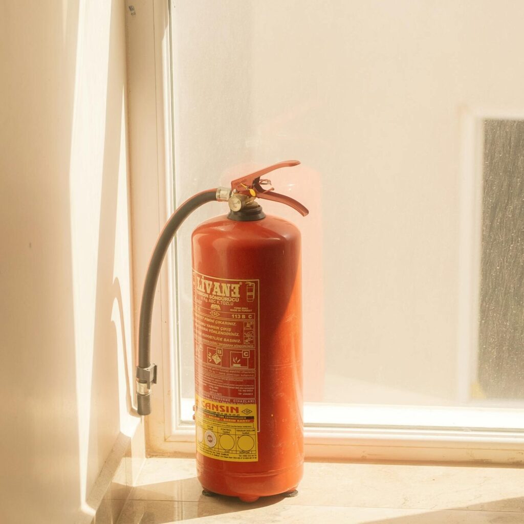 A red fire extinguisher placed by a sunlit window on a polished floor.